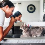 A curious cat watching a girl brush her teeth, symbolizing feline bathroom fascination.