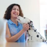 A Dalmatian dog affectionately licks a smiling woman's face, illustrating a common sign of canine affection and bonding between a dog and its owner.