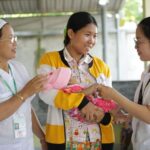 A health worker assisting a young mother and her baby in Cambodia, providing essential care and information on child health and nutrition to combat malnutrition.