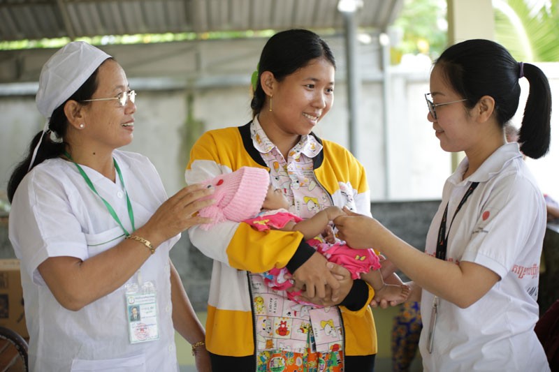 A health worker assisting a young mother and her baby in Cambodia, providing essential care and information on child health and nutrition to combat malnutrition.