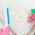 A person wearing pink disposable gloves cleans yellow stains from a white pillow