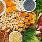 A platter of food containing apricots, peanuts, broccoli and other forods.