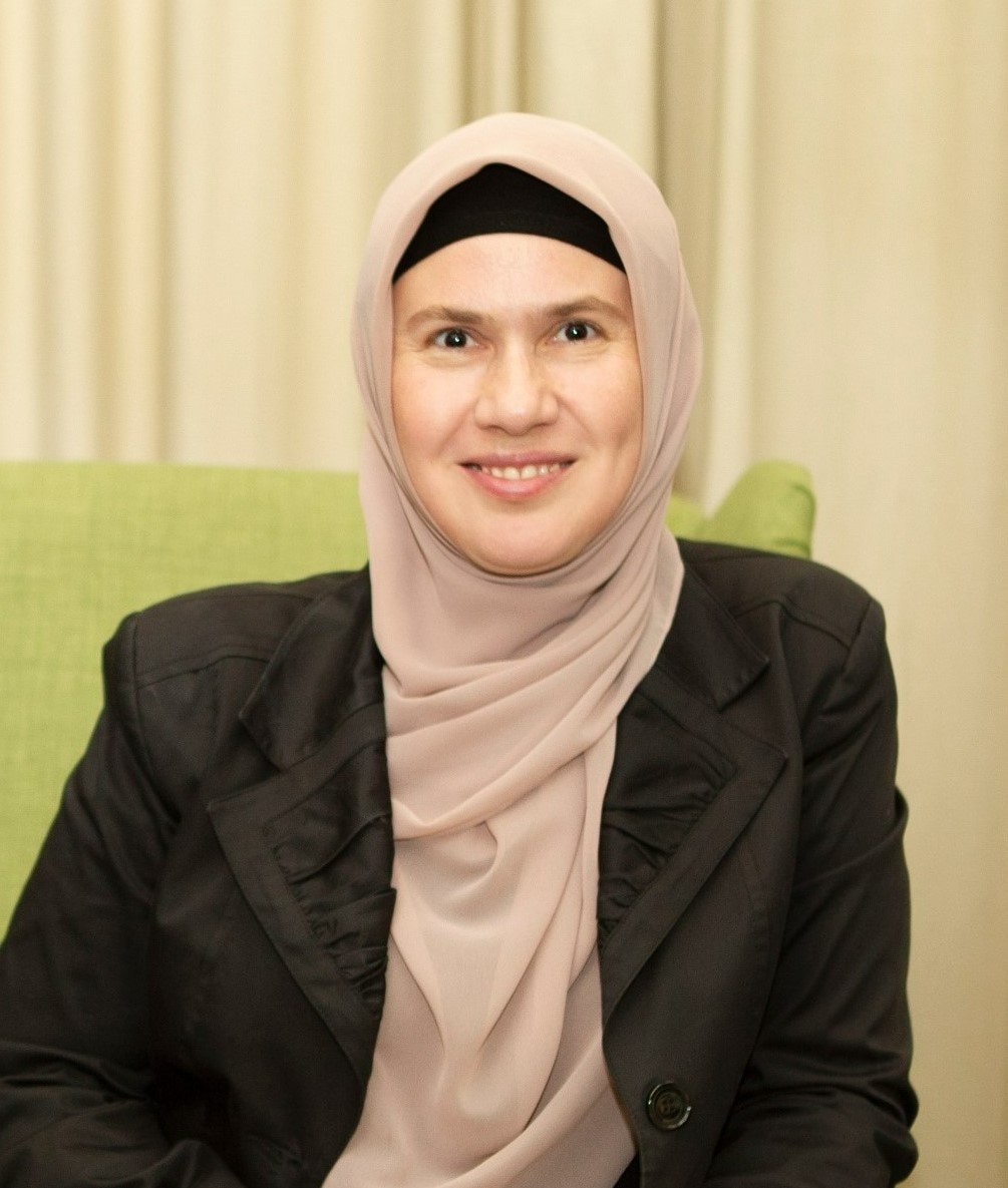 A smiling woman wearing a beige hijab and a black undercap.