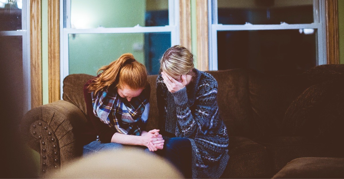 A woman prays with her head bowed on a couch, symbolizing grief and the comfort found in faith, relevant to the Bible verse 'Jesus wept'.