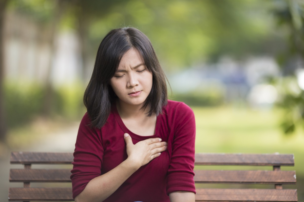 A woman sitting on a park bench experiencing rib cage pain