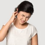 A young woman with impacted ear wax touches her painful ear