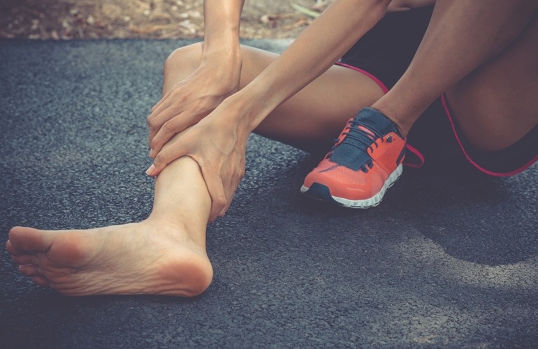 An individual clutches their ankle, illustrating the localized pain associated with a charley horse muscle cramp.