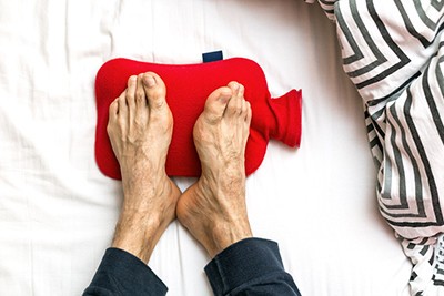 Close-up image of cold feet sticking out from under a warm duvet, illustrating the common experience of freezing feet at night.