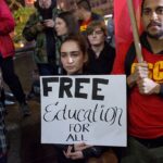 College students advocate for free education during a campus protest, holding signs that read 'Education is a right! Free Education Now!'