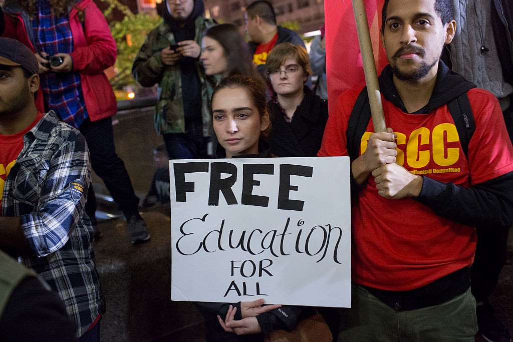 College students advocate for free education during a campus protest, holding signs that read 'Education is a right! Free Education Now!'