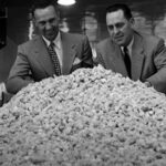 Founders of Taffy Town stand behind a large mound of salt water taffy, showcasing the scale of their candy production and history.