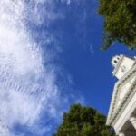 Looking up at Gilman Hall clock tower with blue skies and white clouds