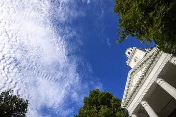 Looking up at Gilman Hall clock tower with blue skies and white clouds