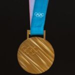 Olympic gold medal with the 5 Olympian rings engraved on it, hanging on a blue ribbon also with the rings