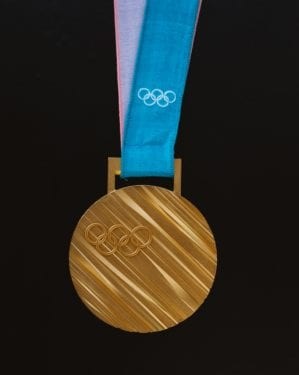 Olympic gold medal with the 5 Olympian rings engraved on it, hanging on a blue ribbon also with the rings