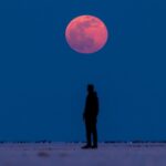 Person standing looking at the blood moon above during a total lunar eclipse