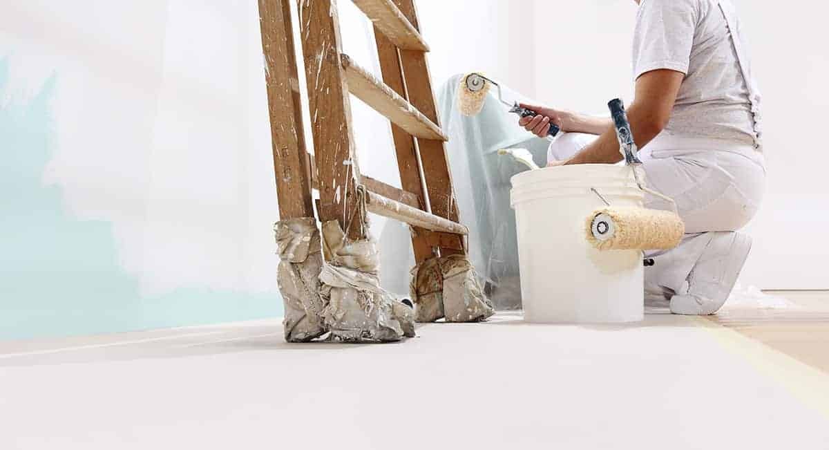 Professional painter in white uniform using a paint roller on a house exterior