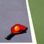 Simple geometric image of a pickleball and pickleball paddle laying on the corner of a colorful pickleball court.