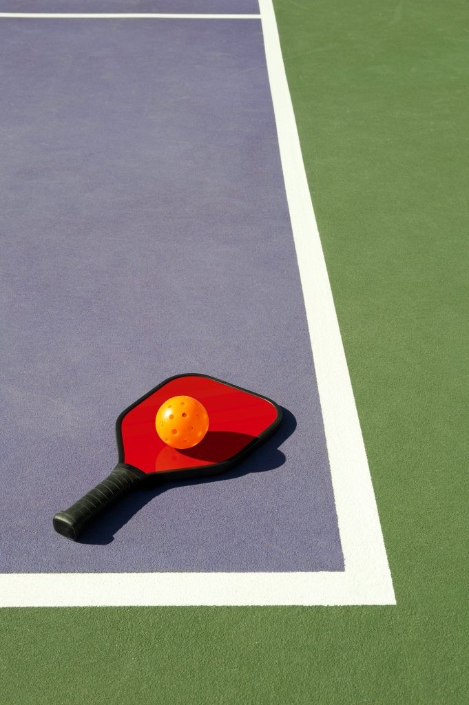 Simple geometric image of a pickleball and pickleball paddle laying on the corner of a colorful pickleball court.