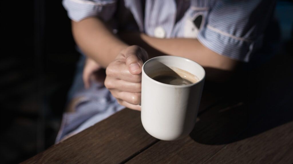 Steaming coffee mug held in hand, symbolizing the need for caffeine to overcome morning tiredness.