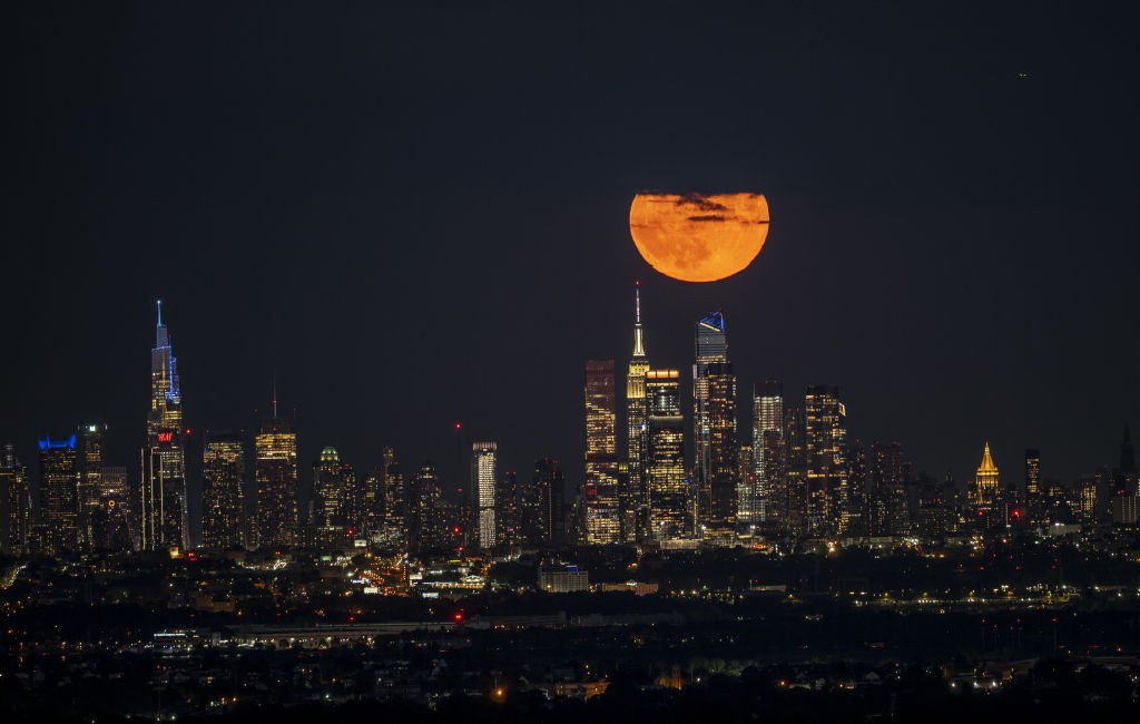 The 1 August 2023 supermoon captured by Fatih Aktas, New York City, USA. The image displays the moon in a bright orange color above the Empire State Building due to atmospheric scattering.