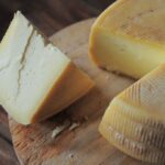 Wedge of cheese cut from a larger wheel; sitting on top of a wooden cutting board