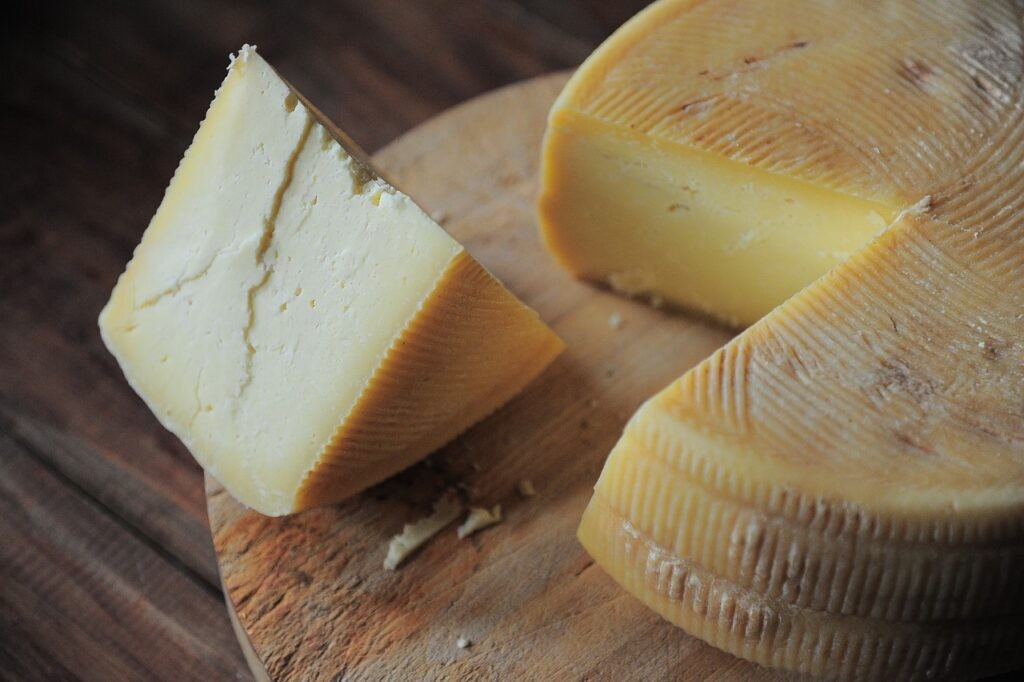 Wedge of cheese cut from a larger wheel; sitting on top of a wooden cutting board