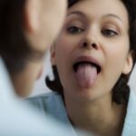 Woman examining her white tongue in mirror, checking for oral health issues and white tongue conditions