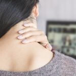 Woman experiencing neck pain when turning head, holding the back of her neck for relief.