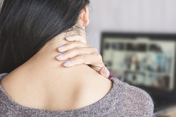 Woman experiencing neck pain when turning head, holding the back of her neck for relief.