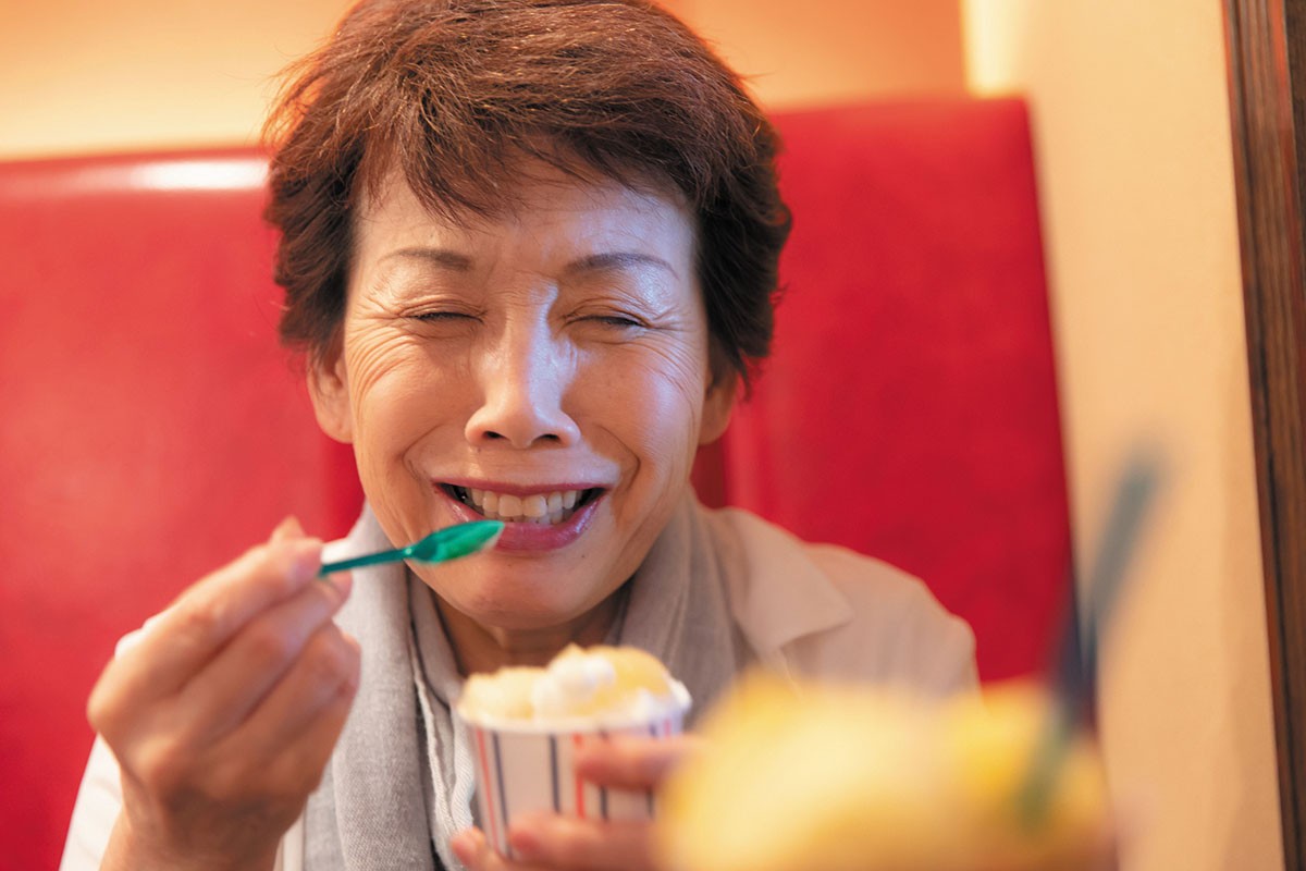 Woman grimacing and holding her forehead after experiencing brain freeze from eating ice cream, illustrating the sudden intense headache caused by rapid consumption of cold treats