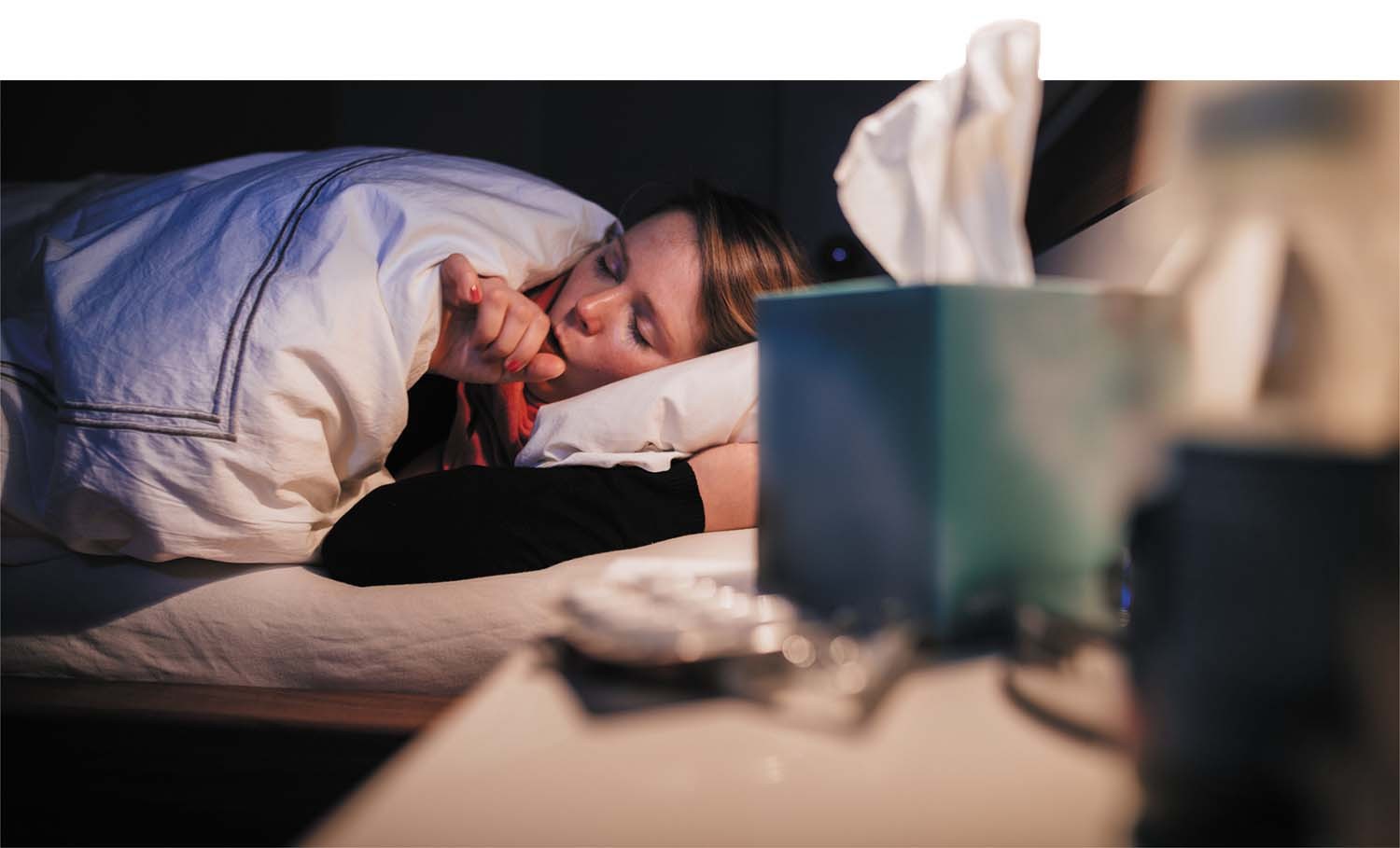 Woman in bed with cold experiencing nighttime symptoms, tissues and cold medicine on nightstand.