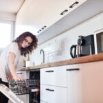 Woman loading dishes into an energy-efficient dishwasher, highlighting the use of modern appliances to reduce electricity consumption.