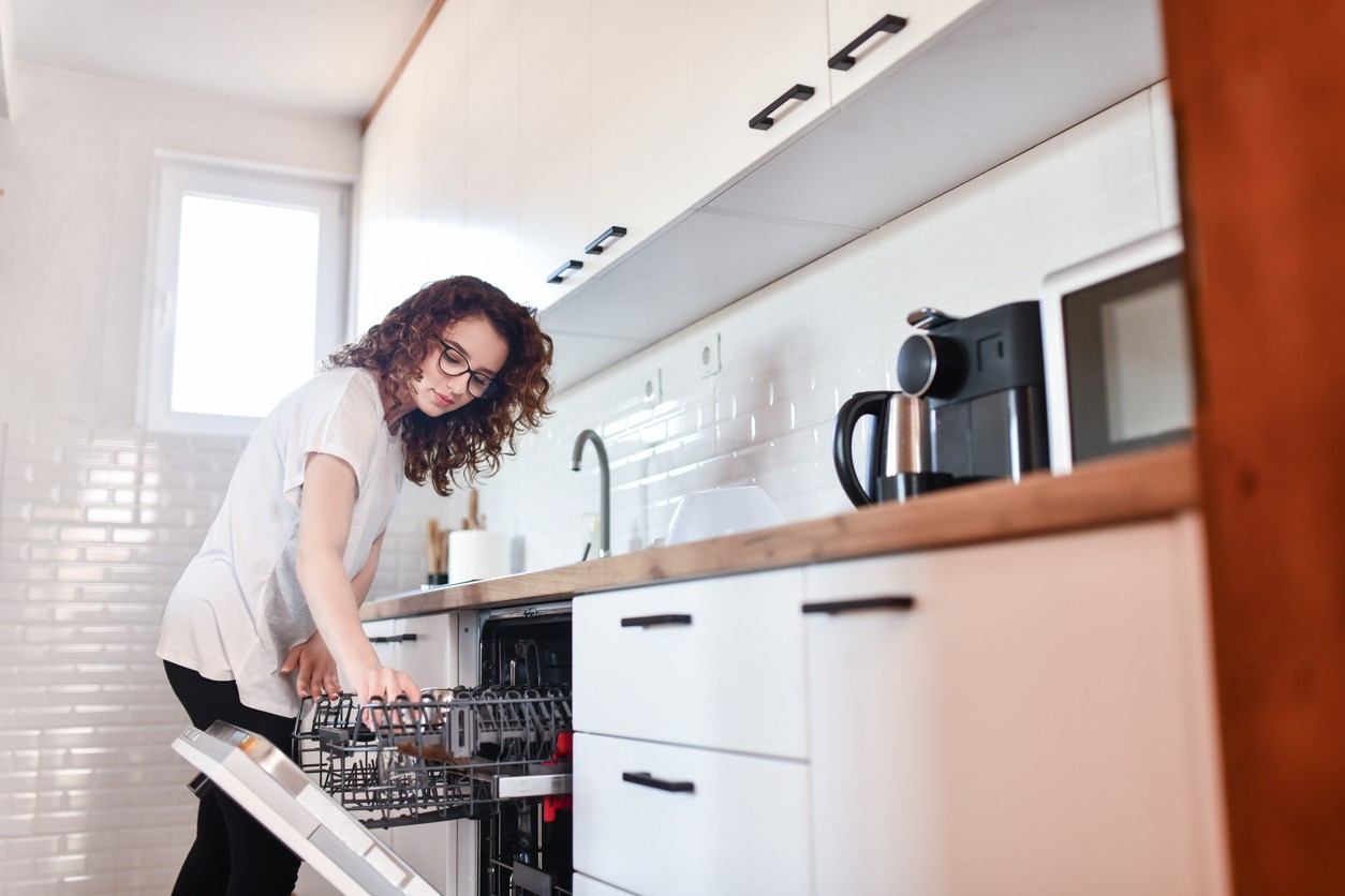 Woman loading dishes into an energy-efficient dishwasher, highlighting the use of modern appliances to reduce electricity consumption.