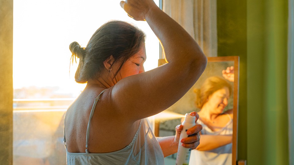 Woman thoughtfully examining her armpit in a mirror while considering deodorant options, highlighting potential skin sensitivity.