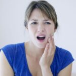 Worried woman holds her jaw in pain indicating jaw popping and TMJ disorder