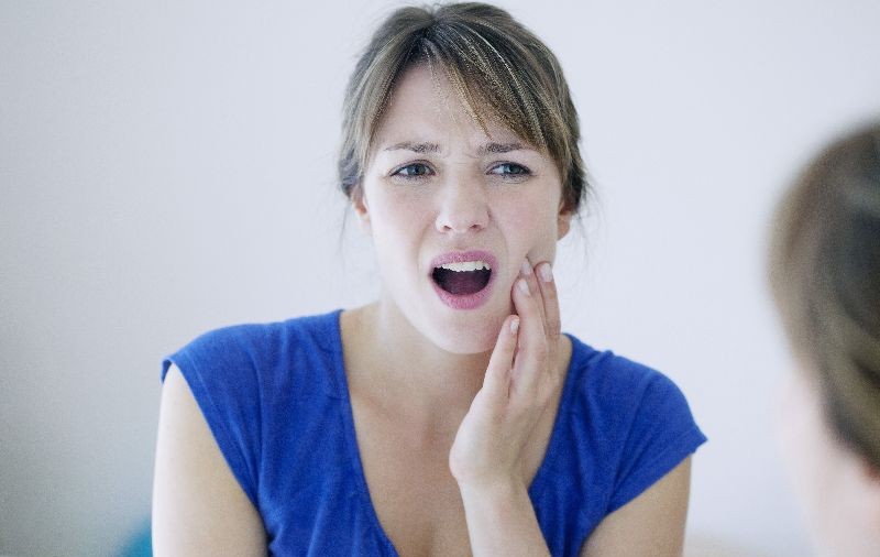 Worried woman holds her jaw in pain indicating jaw popping and TMJ disorder