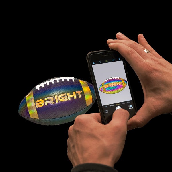 A person holding a reflective football, demonstrating how it lights up under the camera flash, emphasizing the flash's crucial role in activating the reflective material.