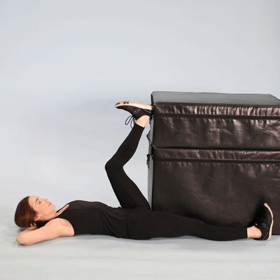 A woman lying on the floor stretching a leg up a large block.