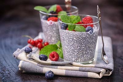 A top-down view of two mason jars filled with chia seed pudding, garnished with fresh raspberries, blueberries, and a sprig of mint, sitting on a rustic wooden surface