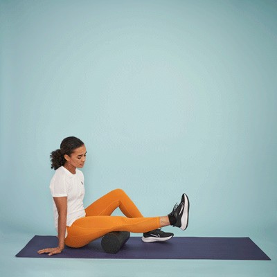 Woman sitting on the floor with one leg outstretched on a foam roller moving backward and forward