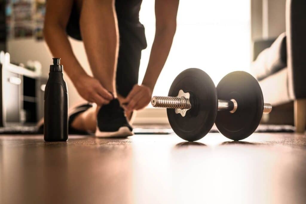 Someone working out tying their shoe with a barbell visible.