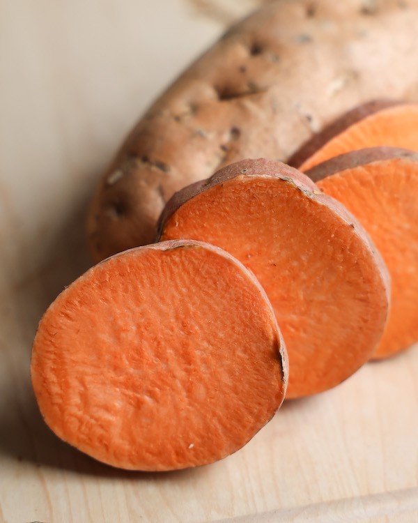 A close-up of a sliced baked sweet potato showing the vibrant orange flesh